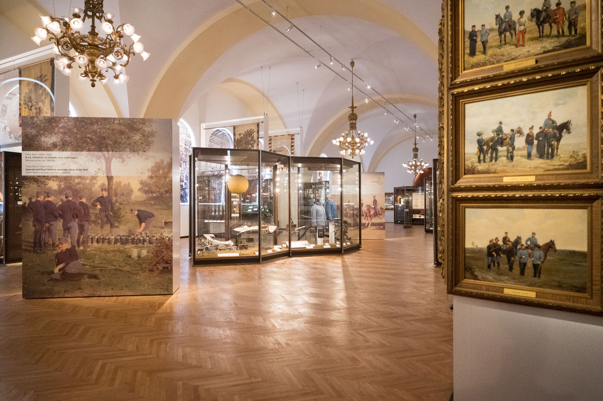 Diese Aufnahme zeigt den Franz-Josef-Saal im Heeresgeschichtlichen Museum in Wien. Die Ausstellung präsentiert eine Sammlung von Artefakten, Uniformen und historischen Waffen aus der Zeit der Habsburgermonarchie von 1867 bis 1918. Im Zentrum der Ausstellung steht eine große Informationstafel mit einer Karte der Habsburgermonarchie und Beschreibungen der wichtigsten historischen Ereignisse und Regionen. Die Vitrinen rundherum zeigen detaillierte Exponate, darunter militärische Kleidung und Ausrüstungen, die die Besucher in die Geschichte dieser Ära eintauchen lassen.