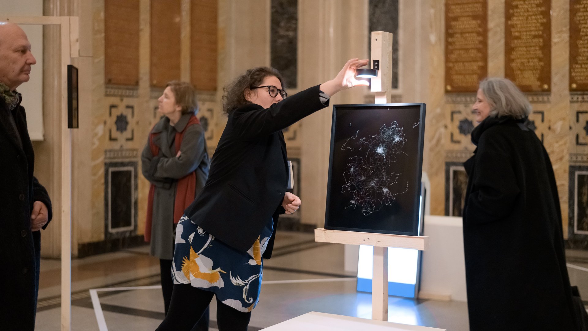 Auf diesem Bild sieht man die Künstlerin Raffaela Bielesch vor einem Bild mit schwarzen Hintergrund, dekoriert mit Düppel-Streifen. 