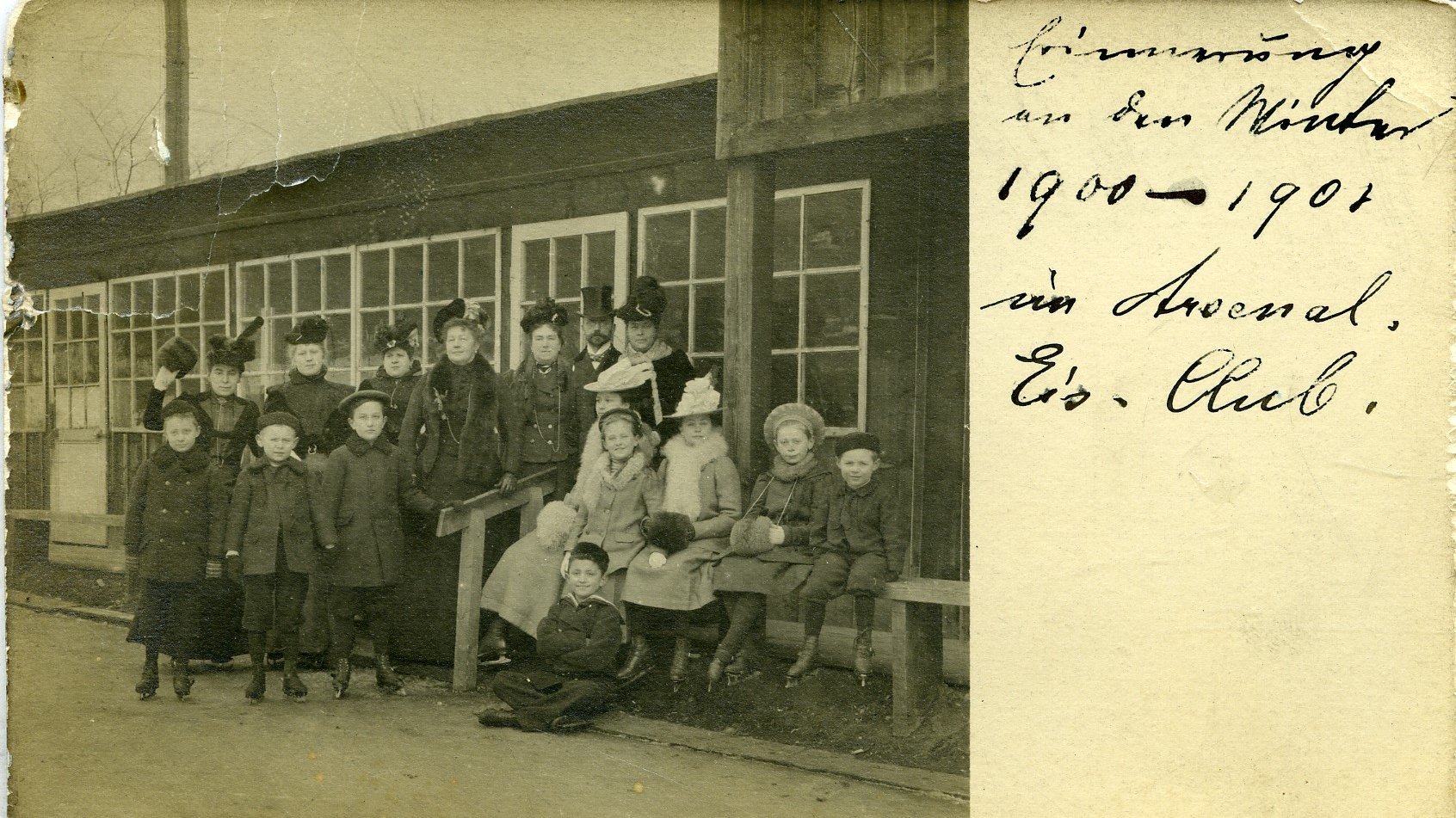 Das Bild zeigt eine Gruppe von Kindern und Erwachsenen, die in warmer Winterkleidung vor einem Holzgebäude mit großen Fenstern posieren. Die meisten tragen Mäntel, Hüte und Muffs, passend zur kalten Jahreszeit. Es scheint eine Winteraktivität oder ein Treffen im Freien zu sein. Die handschriftliche Notiz auf der rechten Seite des Bildes lautet: „Erinnerung an den Winter 1900 - 1901 im Arsenal, Eis. Club.“, was darauf hindeutet, dass es sich um eine Erinnerung an ein Ereignis aus dieser Zeit handelt, vermutlich in einem Eislaufclub.