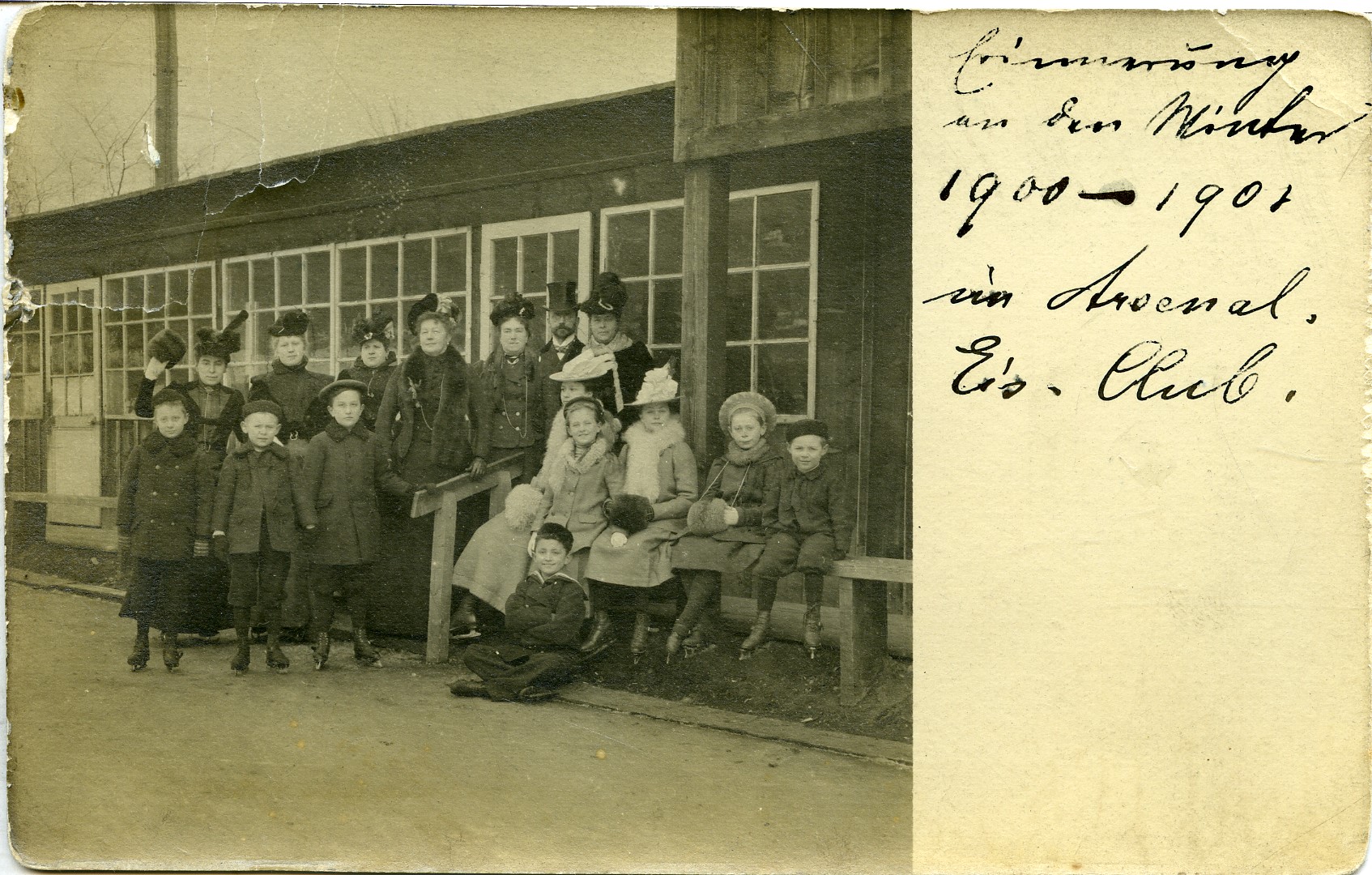 Das Bild zeigt eine Gruppe von Kindern und Erwachsenen, die in warmer Winterkleidung vor einem Holzgebäude mit großen Fenstern posieren. Die meisten tragen Mäntel, Hüte und Muffs, passend zur kalten Jahreszeit. Es scheint eine Winteraktivität oder ein Treffen im Freien zu sein. Die handschriftliche Notiz auf der rechten Seite des Bildes lautet: „Erinnerung an den Winter 1900 - 1901 im Arsenal, Eis. Club.“, was darauf hindeutet, dass es sich um eine Erinnerung an ein Ereignis aus dieser Zeit handelt, vermutlich in einem Eislaufclub.